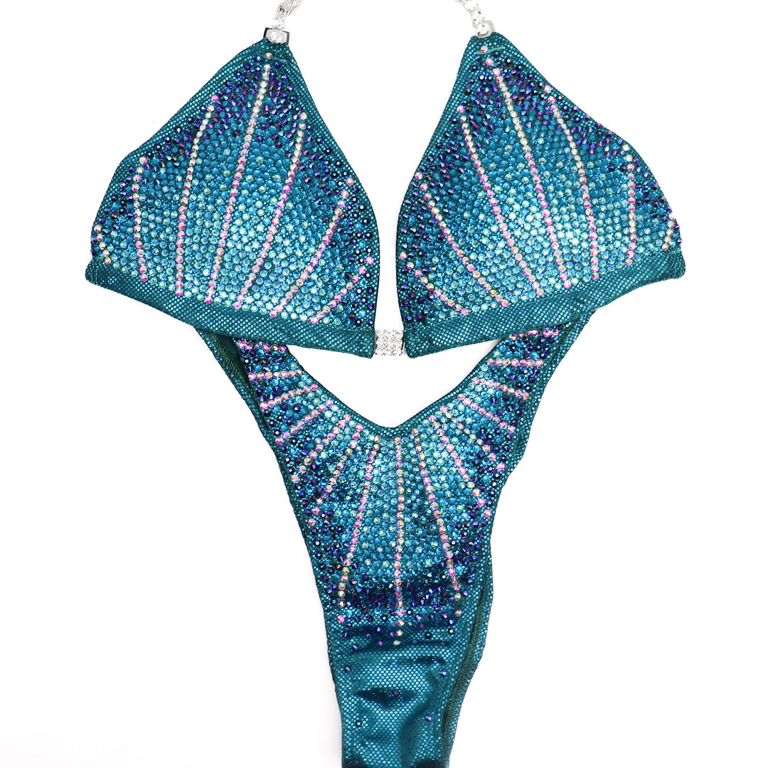  The Teal Cosmo Competition Suit, crafted for female Figure Competitors. Dive into the Cosmos with its mesmerizing teal hue, exuding power and elegance. Engineered for peak performance and style, this suit guarantees to command attention on stage. Dominate the competition with confidence in every pose.