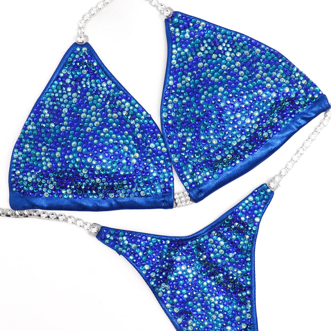 The Blue Shimmer Crystal Radiance competition suit for NPC Bikini or Wellness competitors. Dazzle on stage with its captivating blue sparkle and crystal embellishments. Command attention with elegance and confidence. Elevate your performance and shine like never before.