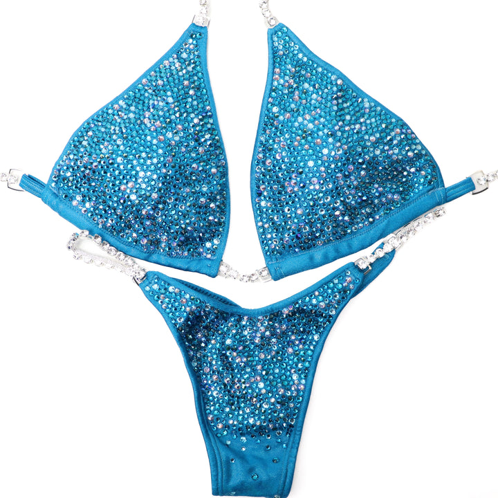 Shine with Kerigan's Turquoise Radiance! 💙 This breathtaking turquoise competition suit dazzles with blue-toned crystals and a touch of Emerald AB for a unique green sparkle. Elevate your stage presence and sparkle like never before with Kerigan Pike! ✨🏆 #Bodybuilding #CompetitionSuit #TurquoiseRadiance #FitnessFashion #StageGlam