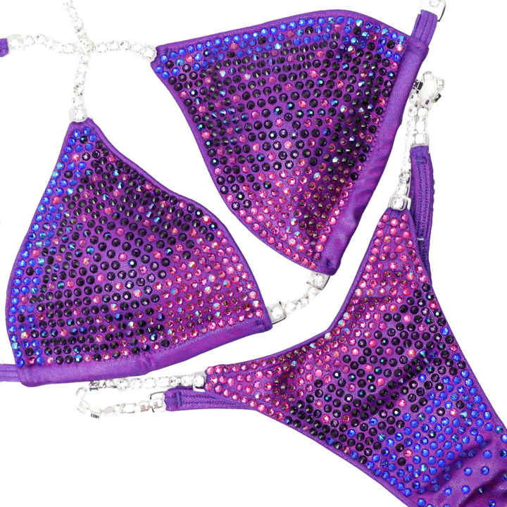 Introducing Courtney's Arnold Purple Candy Trinity, a show-stopping competition suit for female bodybuilders. Adorned with fuchsia and purple crystals, it lights up the stage, boosting confidence with every pose. Unleash your inner strength and elegance in this stunning ensemble. Work the stage with Courtney Starr!
