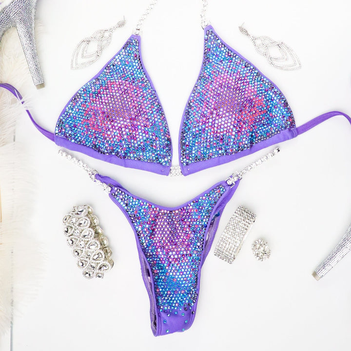 Introducing Deb's Lilac Lollipop Nova, a one-of-a-kind suit for female bodybuilders. Radiating in lilac with vibrant pinks, blues, and purples, it guarantees to make you stand out on stage. Own your spotlight with this unique masterpiece! 💪🎉 #FemaleBodybuilding #StandOutStyle