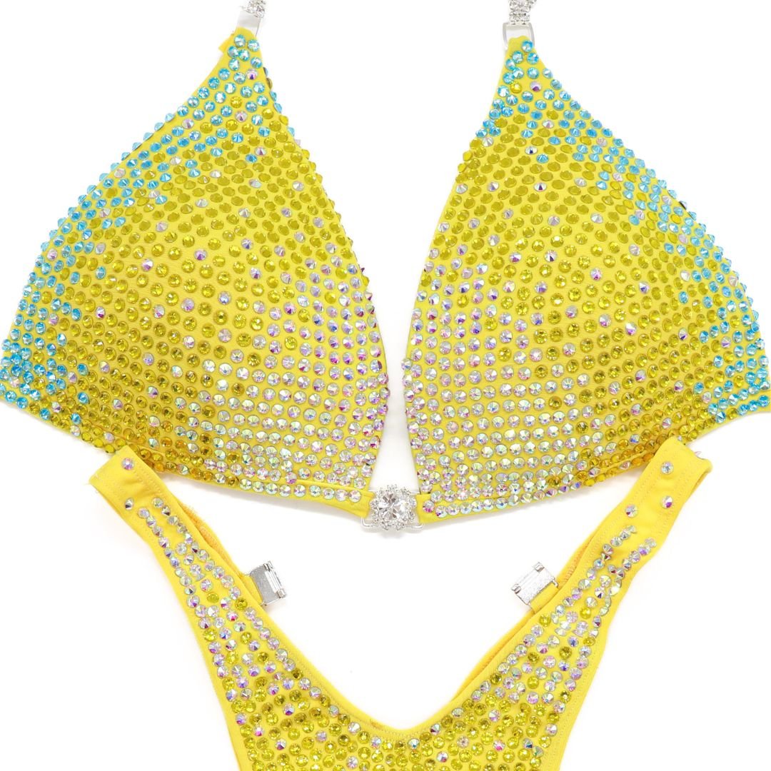 Yellow custom bikini set adorned with blue, pink, and clear gradient crystals for athletes and figure competitors.