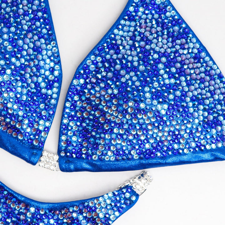 "Get ready to shine with Mary Ann's Royal Radiance! 💙✨ This electric blue bodybuilding suit, featuring captivating blue and color-changing crystals, is designed to make you stand out on stage. Created by Mary Ann Parks for champions who dare to dazzle! #BodybuildingRoyalty #StageGlow #MaryAnnParksDesign"