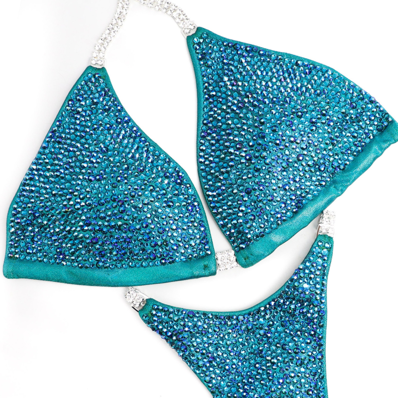 Introducing Casey's Blue Zircon Radiance, a competition suit designed for the fierce female bodybuilder. Inspired by Casey Samsel, its teal and blue hues illuminate the stage with shimmer. Perfect for NPC Bikini or Wellness competitors, this suit exudes confidence and elegance, ensuring you stand out with every pose.
