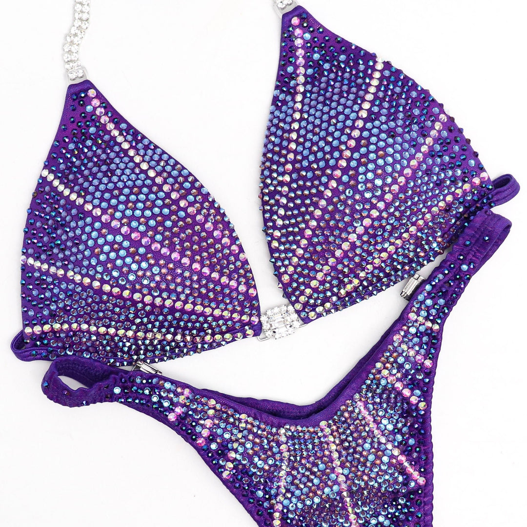 Introducing Purple Lagoon Cosmo 💜! This captivating purple competition suit features a mesmerizing design with purple and crystal burgundy crystals, ensuring you shine brightly on stage with elegance and grace ✨. #Bodybuilding #CompetitionSuit #PurpleLagoonCosmo 👙💎🌟